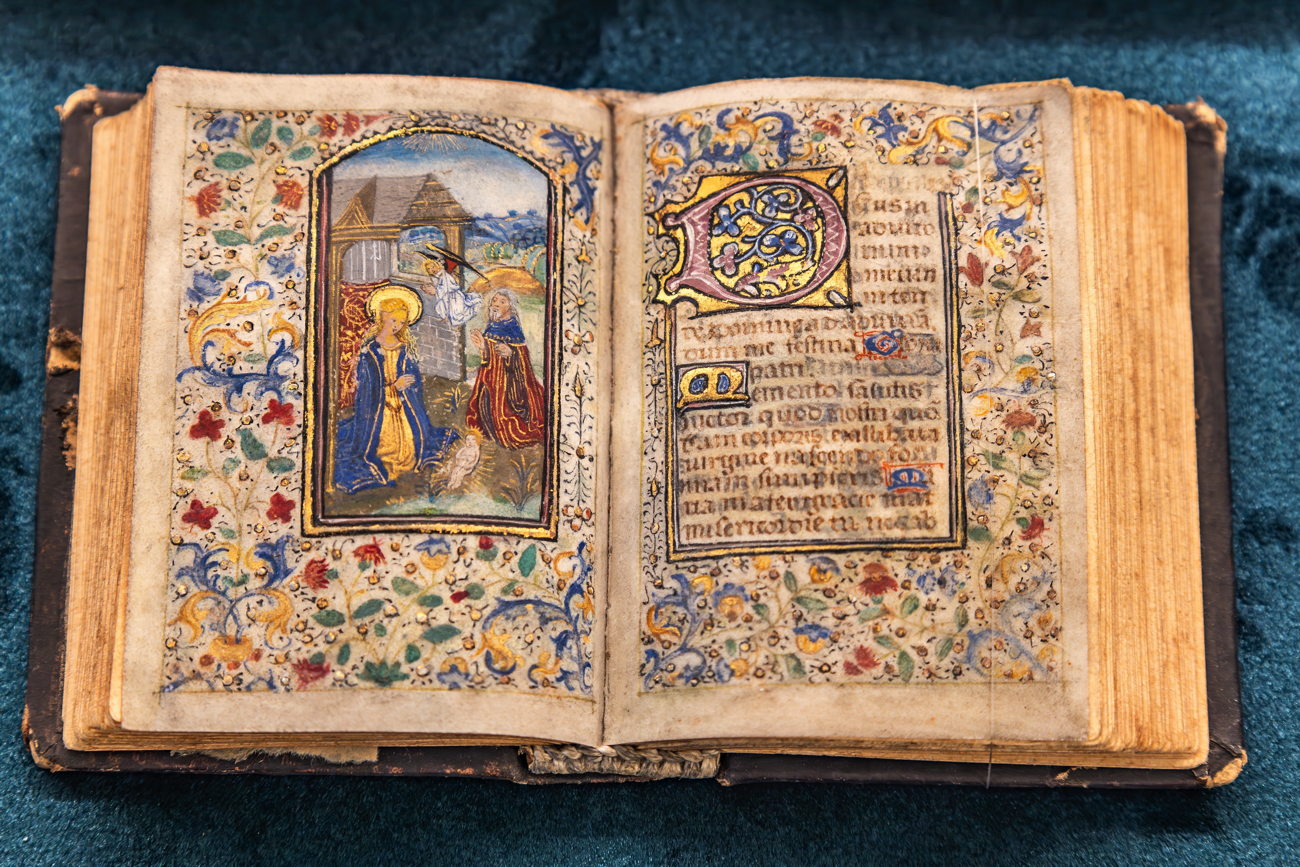 Illuminated book of hours open at a painted miniature, with a gold-leaf initial and floral borders